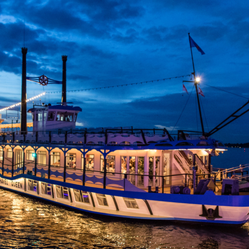 Ein Schiff fährt bei Anbruch der Dämmerung beleuchtet über einen Fluss.